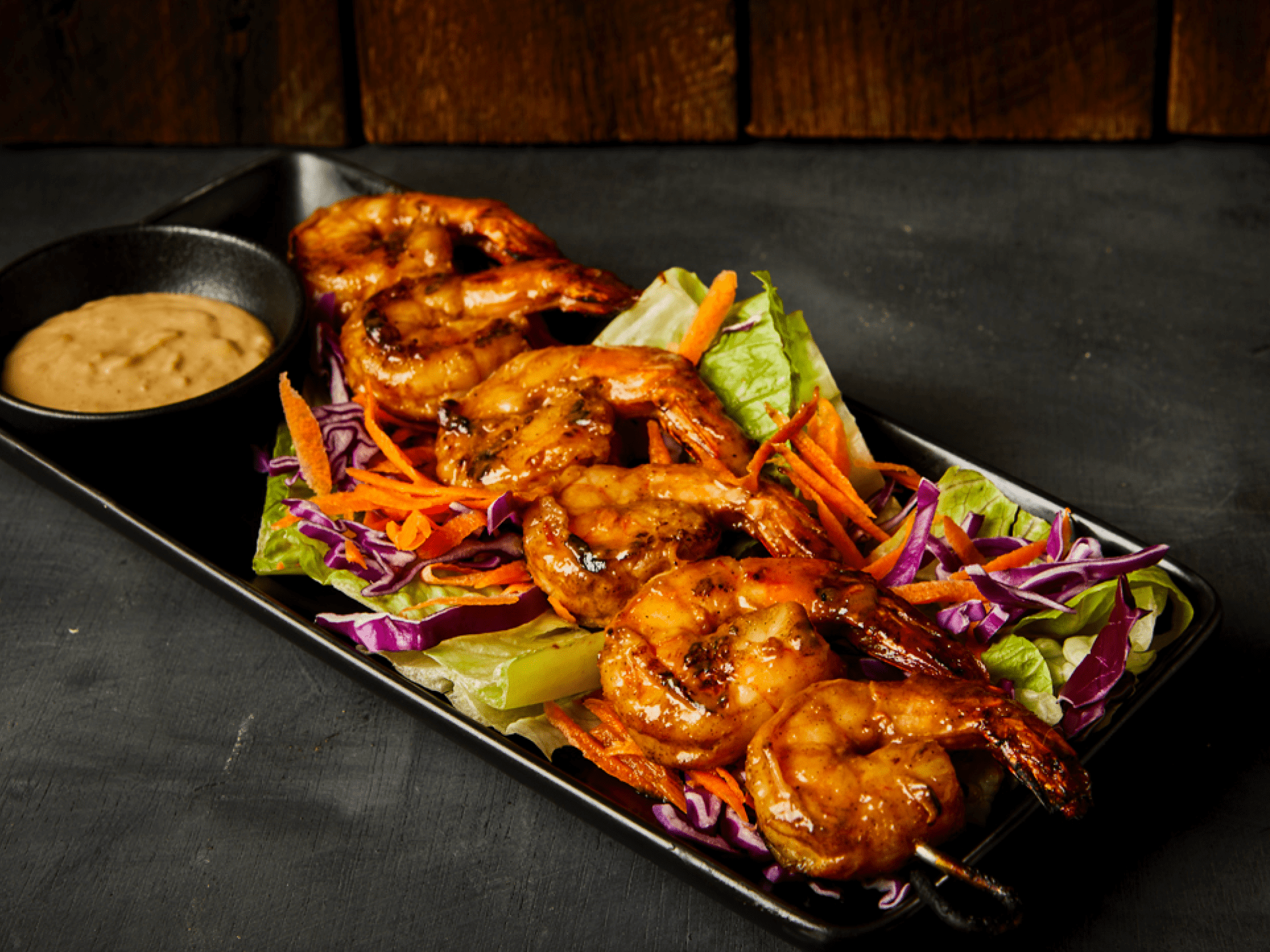 Grilled shrimp skewers on a bed of lettuce, carrots, and cabbage with dipping sauce.