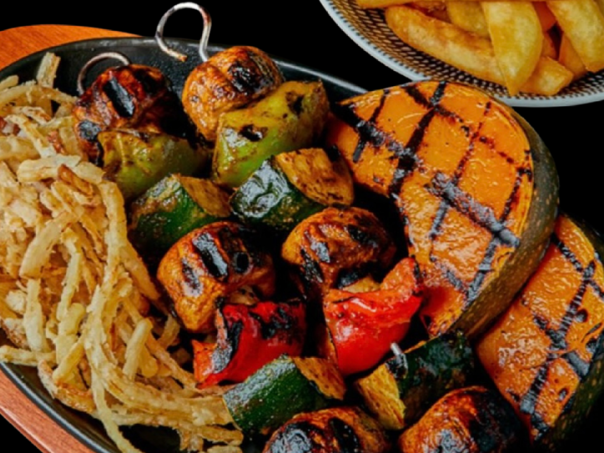 Grilled vegetable skewers, onion rings, and fries on a black background.