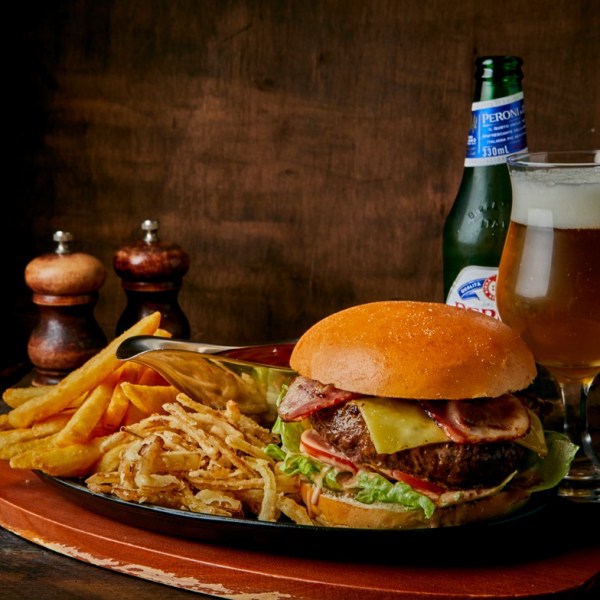 Burger with fries and a glass of beer on a wooden table with salt and pepper shakers.