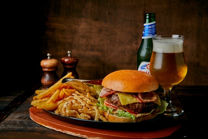 Burger with fries and a glass of beer on a wooden table with salt and pepper shakers.
