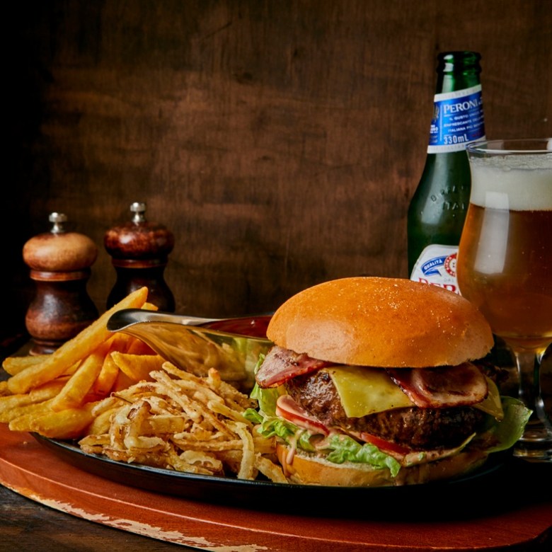 Burger with fries and a glass of beer on a wooden table with salt and pepper shakers.