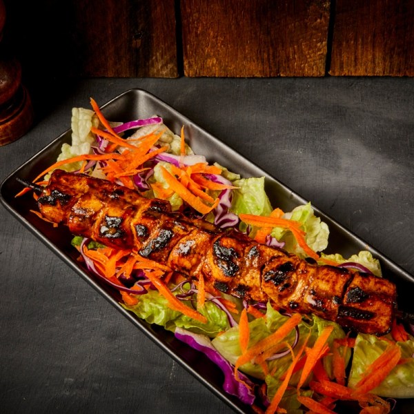 Grilled skewer on a bed of lettuce, carrots, and cabbage in a black rectangular dish.